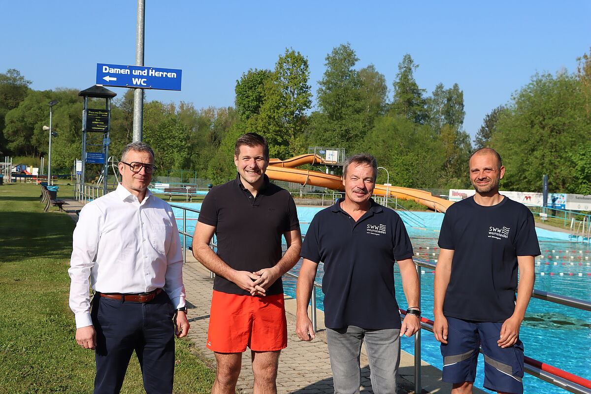 Foto von Marco Krasser, Nicolas Lahovnik, Jürgen Sommerer und Matthias Dollinger, die nebeneinander stehen und in die Kamera lächeln. Im Hintergrund ein Schwimmbecken mit Rutsche.